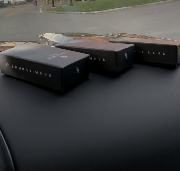 Four Bombay Musk luxury car perfume cartons lined up along a car dashboard